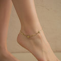Close-up of the gold Dainty Bloom anklet featuring three crystal-centered flowers and a box chain on a white surface.