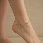 Close-up of the gold Dainty Bloom anklet featuring three crystal-centered flowers and a box chain on a white surface.