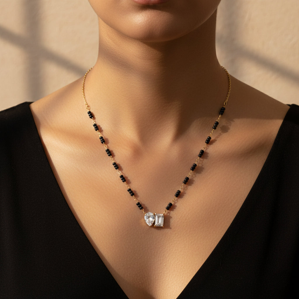 A woman wearing a modern 18K gold-plated mangalsutra featuring black beads and a pendant with one pear-cut and one emerald-cut crystal.
