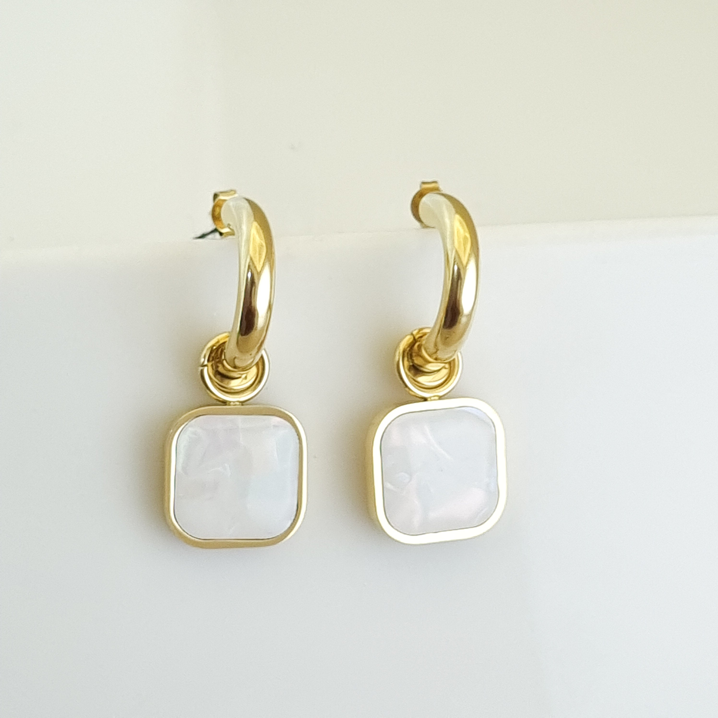 Gold hoop earrings with square white stones on a light background