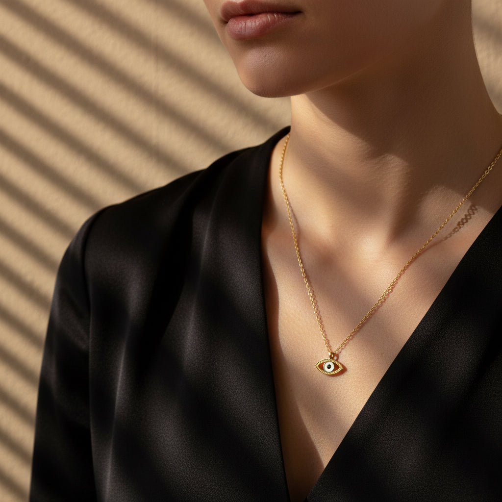 A woman wearing a delicate 18K gold-plated necklace featuring a central Evil Eye pendant with black and white enamel details.