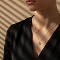A woman wearing a delicate 18K gold-plated necklace featuring a central Evil Eye pendant with black and white enamel details.