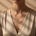A woman wearing a delicate 18K gold-plated double-layered Y-necklace with small spherical gold beads and a larger drop-sphere at the end.