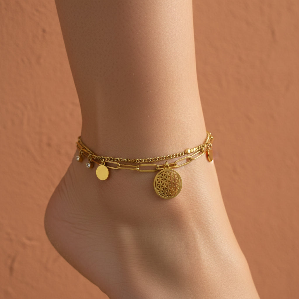 18K gold plated layered anklet featuring a Flower of Life charm, paperclip chain, and gold disc accents on a white surface.