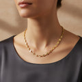 A woman wearing a high-polish 18K gold-plated Marina link chain necklace, styled with a dark grey silk top.