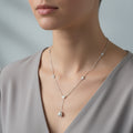 A woman wearing a delicate silver-toned lariat necklace featuring station-set crystals and a central pearl pendant framed by a shimmering halo.