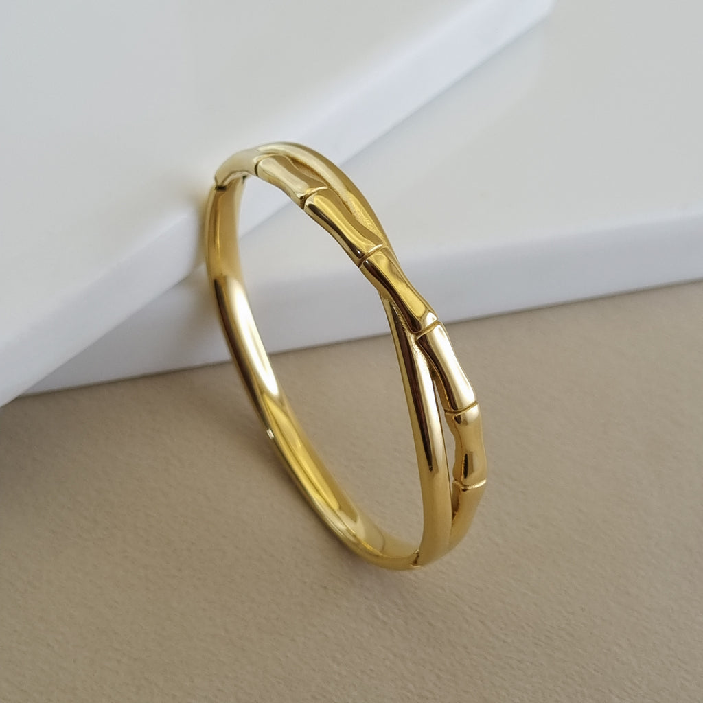 A close-up of an 18K gold-plated bangle designed with organic bamboo-like segments, resting on a minimalist neutral background.