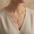 A woman wearing an 18K gold-plated necklace featuring a twisted, organic "molten" style flare pendant on a minimalist neutral background.