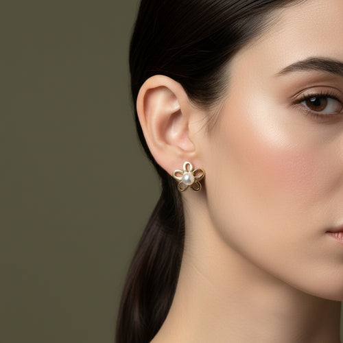 A woman with a sleek ponytail wearing medium-sized, 18K gold-plated five-petal flower stud earrings with a central white pearl.