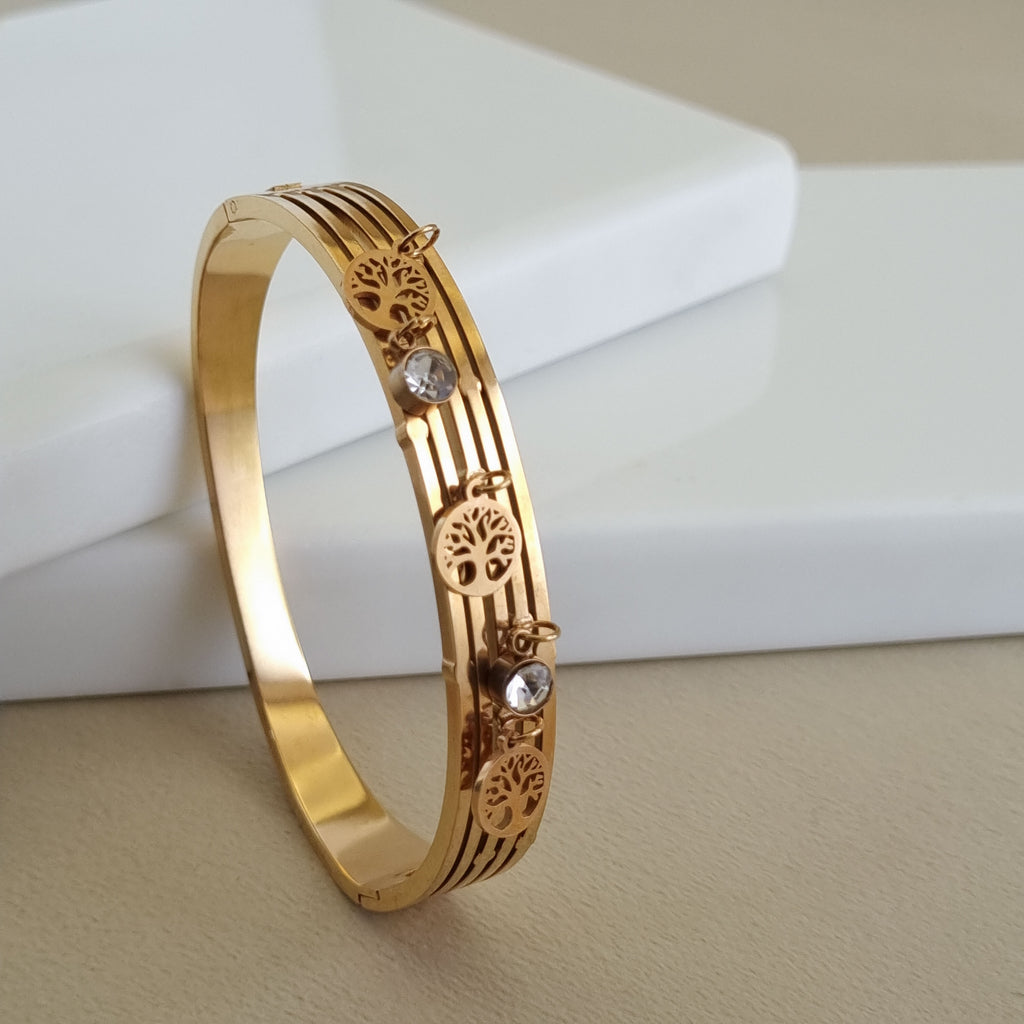 A wide, 4-row 18K rose gold-plated bangle featuring alternating Tree of Life charms and round crystals, displayed horizontally on a neutral background.