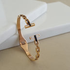 An 18K rose gold-plated open-ended cuff bangle featuring a chain-link design and T-bar terminals with white inlays, displayed on a neutral surface.