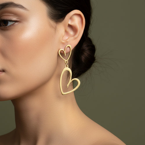 A woman with a sleek bun wearing large, 18K gold-plated open-frame double heart drop earrings with a high-polish finish.