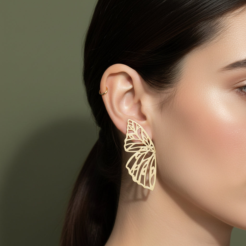 A woman with a sleek ponytail wearing large, 18K gold-plated intricate filigree butterfly wing stud earrings.