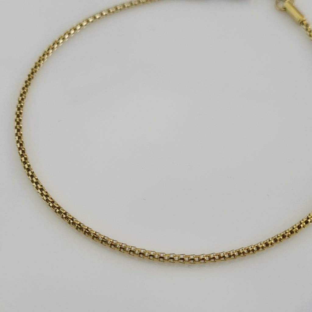 Close-up of an 18K gold plated box chain anklet featuring a smooth geometric design and an adjustable lobster clasp.