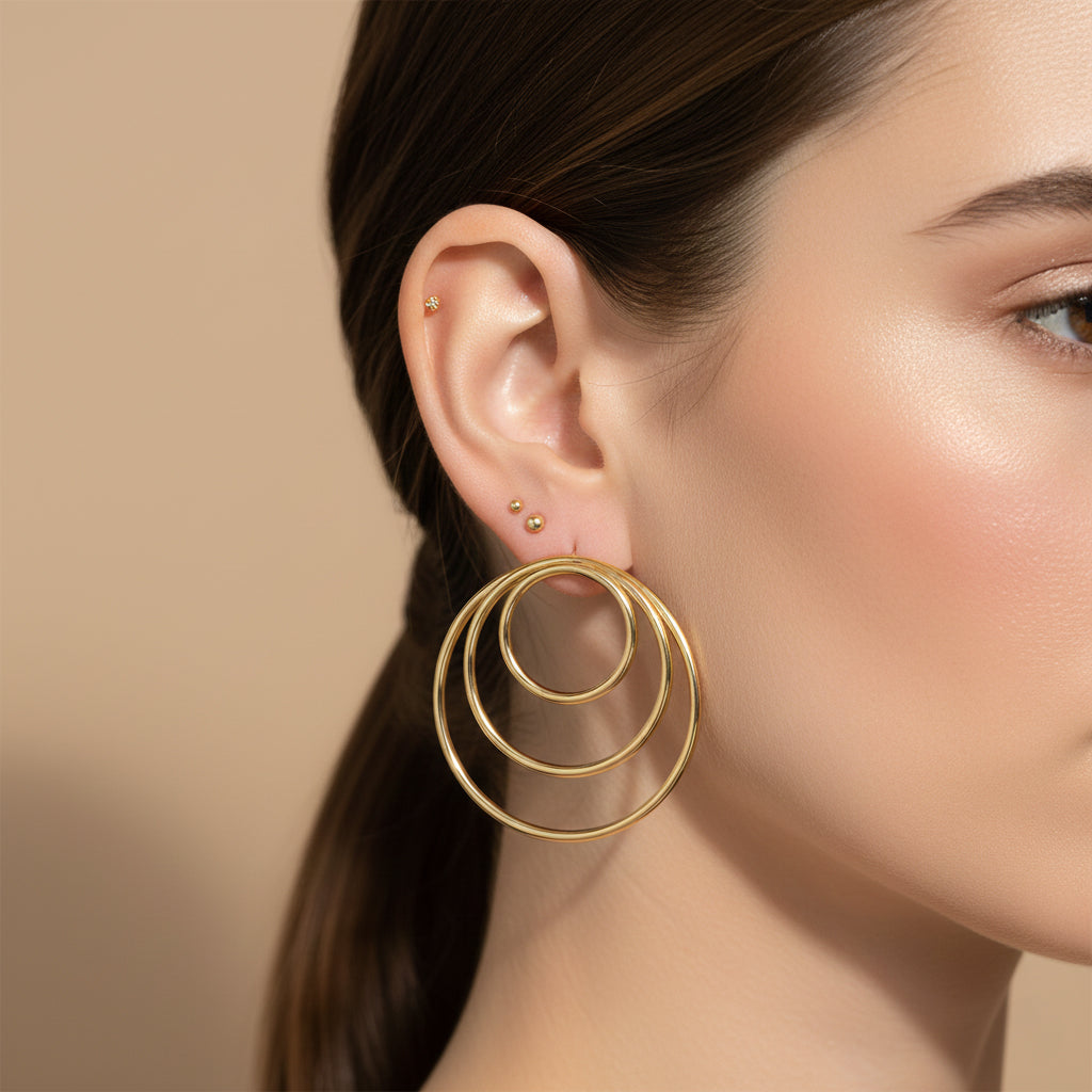 A woman with a sleek ponytail wearing large 18K gold-plated, triple-layered concentric hoop earrings.