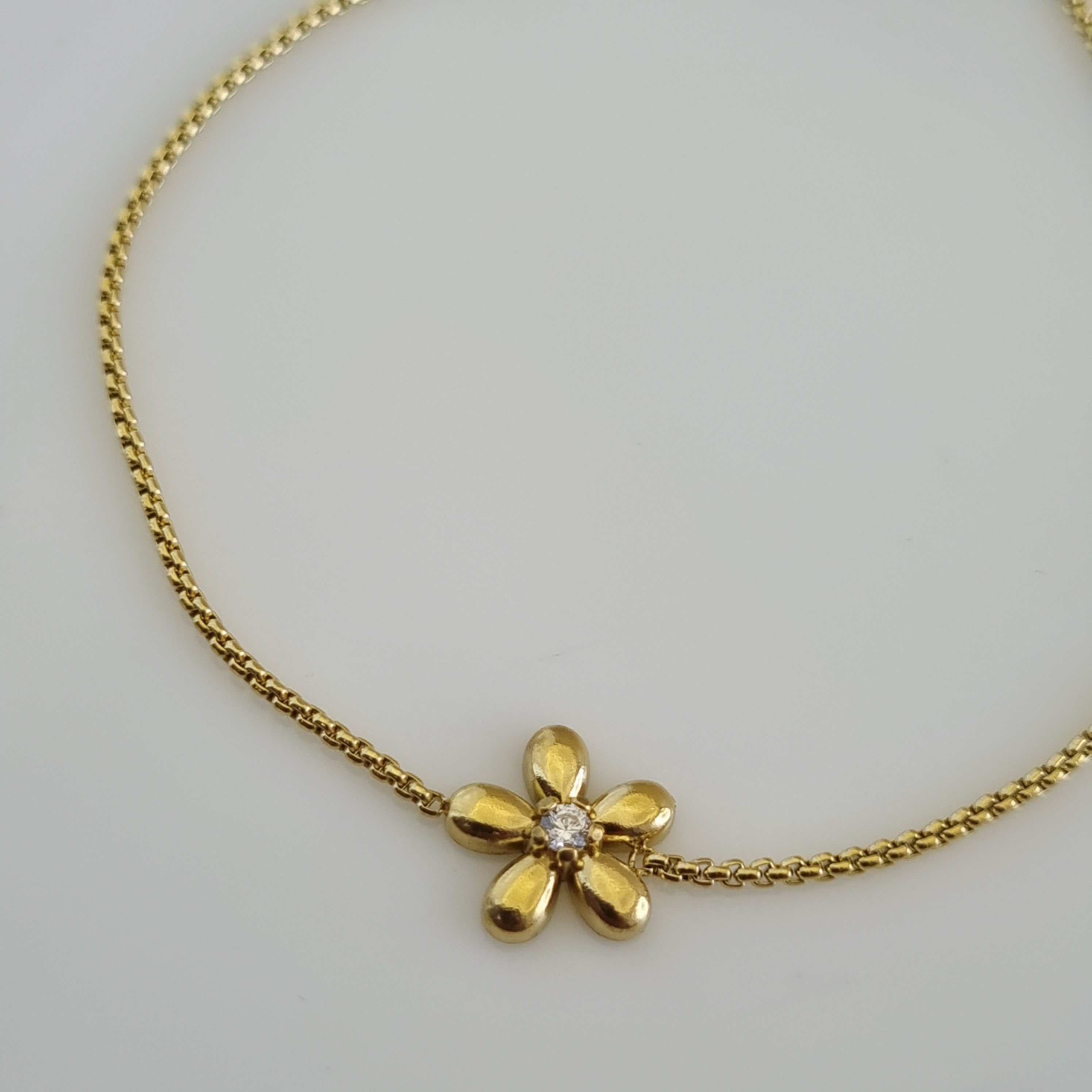 18K gold plated bracelet featuring a small gold flower charm with a crystal center on a micro-box chain.