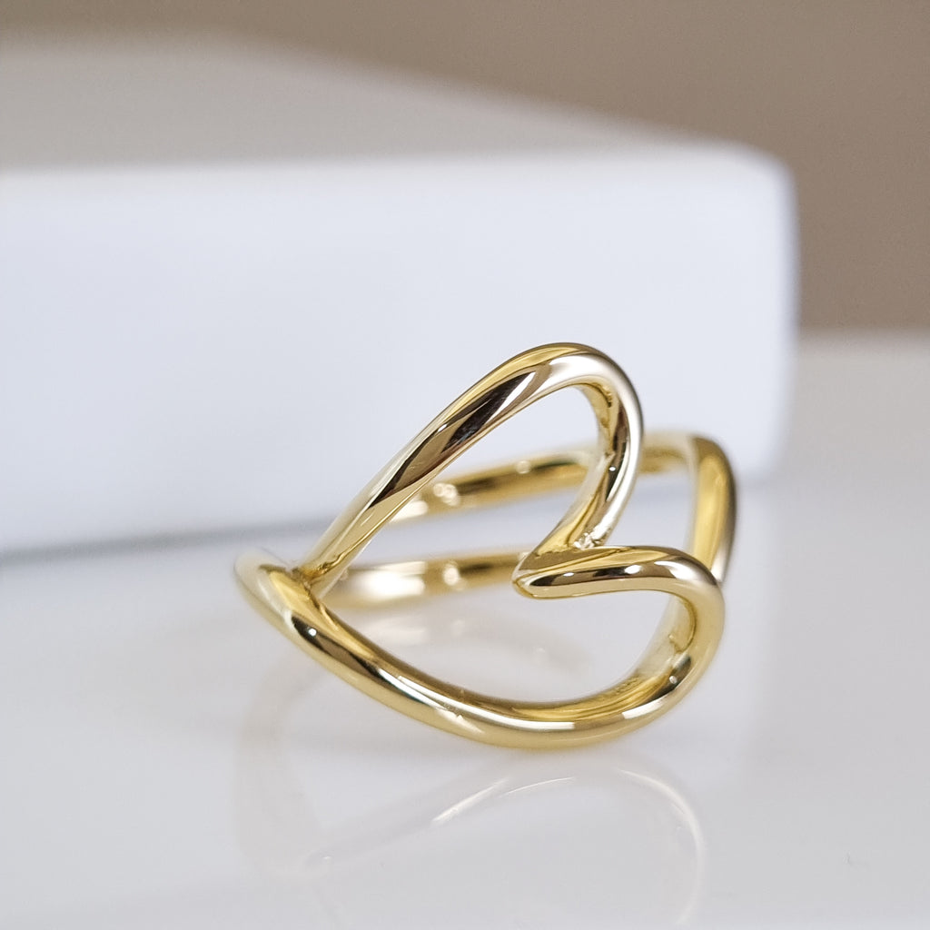 Gold heart-shaped ring on a reflective surface with a neutral background