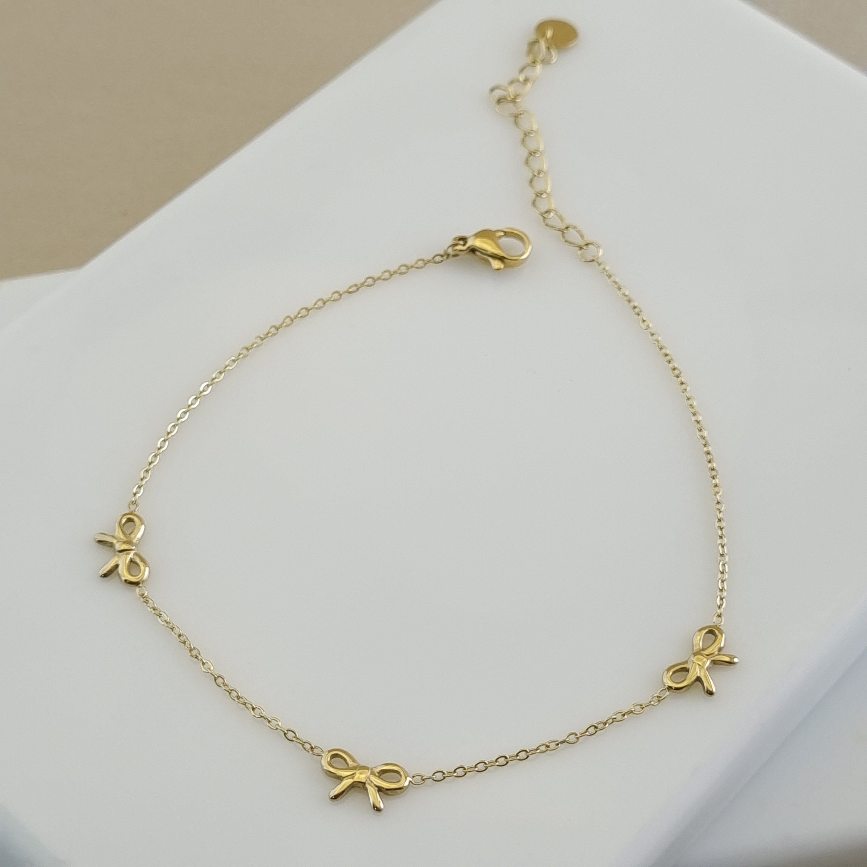Gold anklet with bow-shaped charms on a white surface