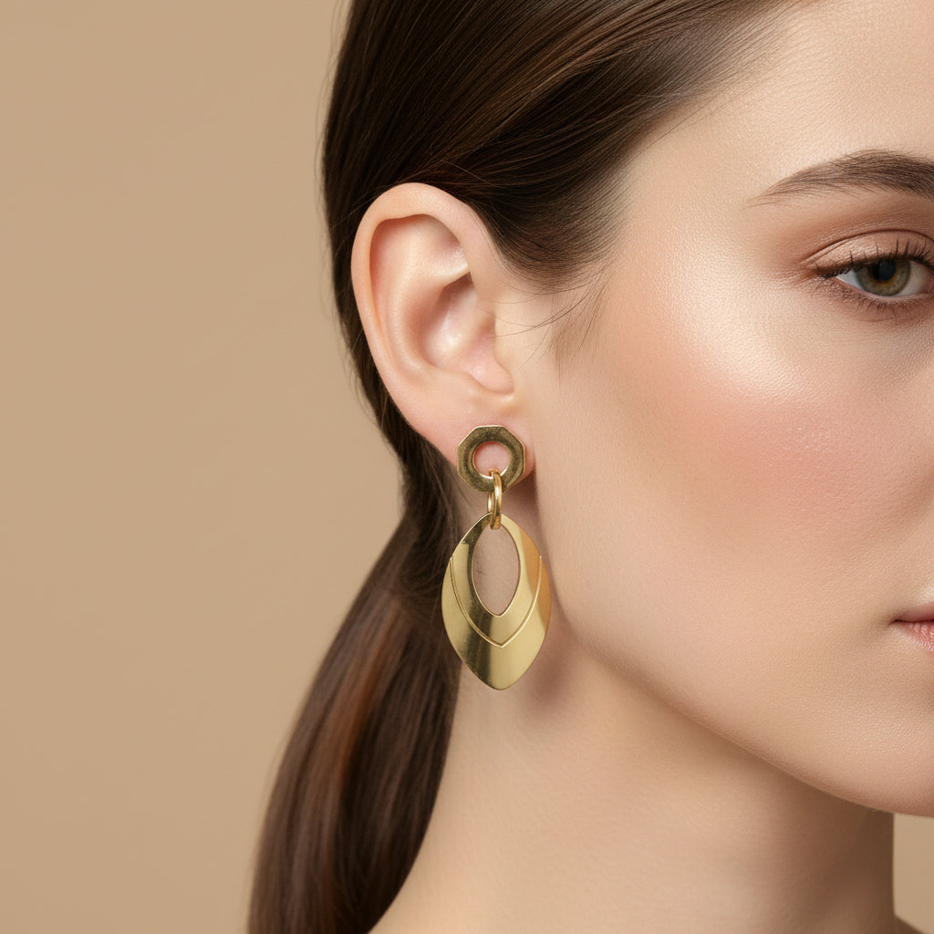 A woman with a sleek low ponytail wearing 18K gold-plated geometric drop earrings featuring a hexagonal top and a tiered marquise-shaped dangle.