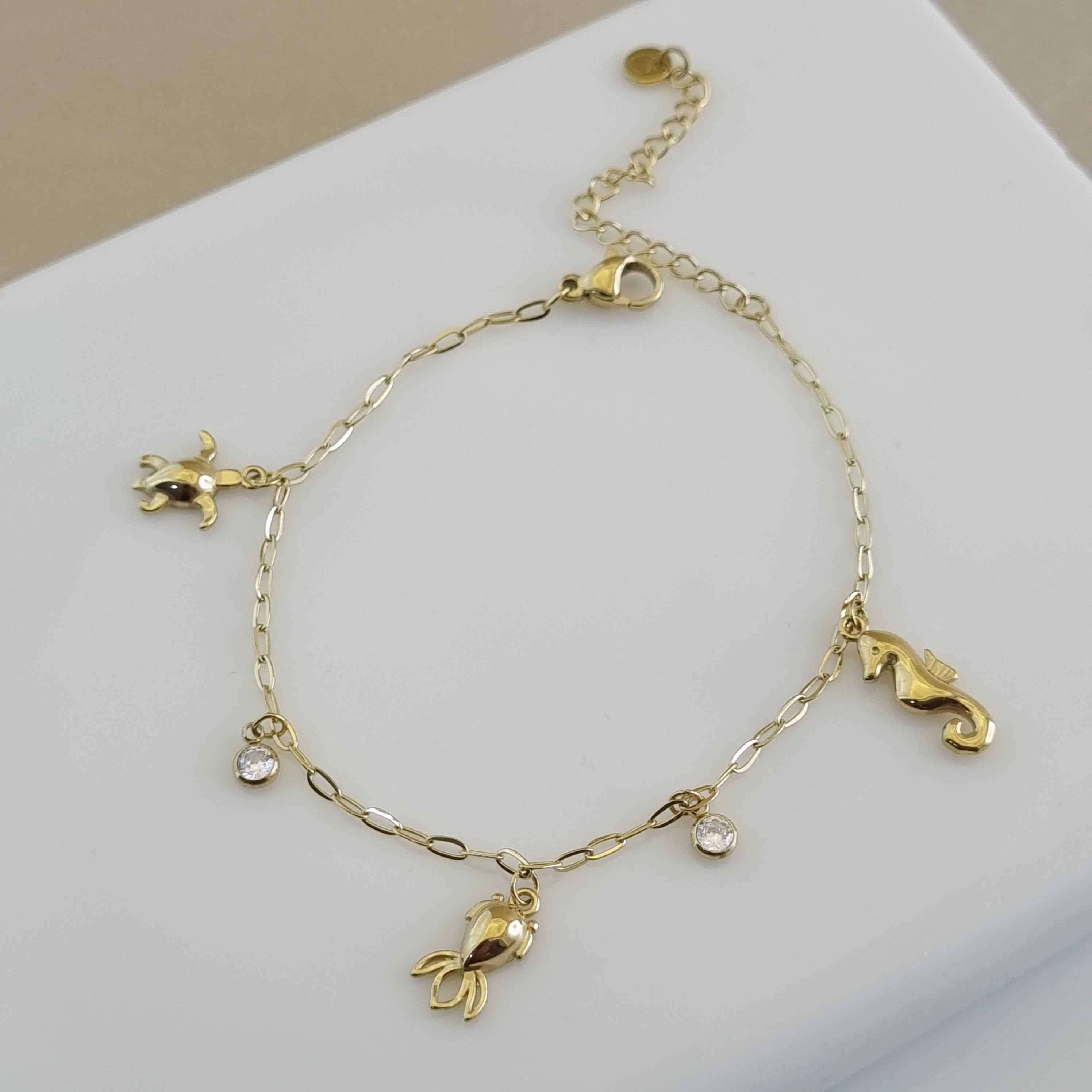 Treshire 18K gold plated bracelet featuring detailed sea turtle, seahorse, and fish charms with bezel crystals on a white display.