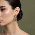 A woman with a sleek hairstyle wearing long, 18K gold-plated fringe drop earrings with a tapered tiered base and cascading fine gold chains.
