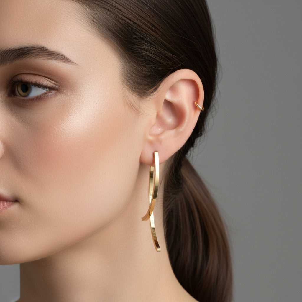 A woman with a sleek ponytail wearing 18K gold-plated vertical beam earrings with a curved architectural design and a high-polish finish.