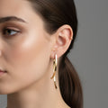 A woman with a sleek ponytail wearing 18K gold-plated vertical beam earrings with a curved architectural design and a high-polish finish.