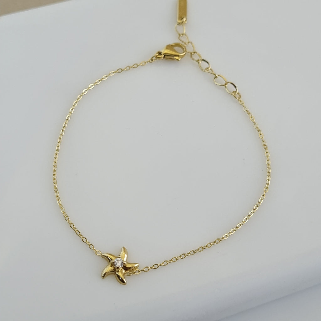 Treshire 18K gold plated Coastal Starfish bracelet with a center crystal on a fine gold chain, displayed on a white marble surface.