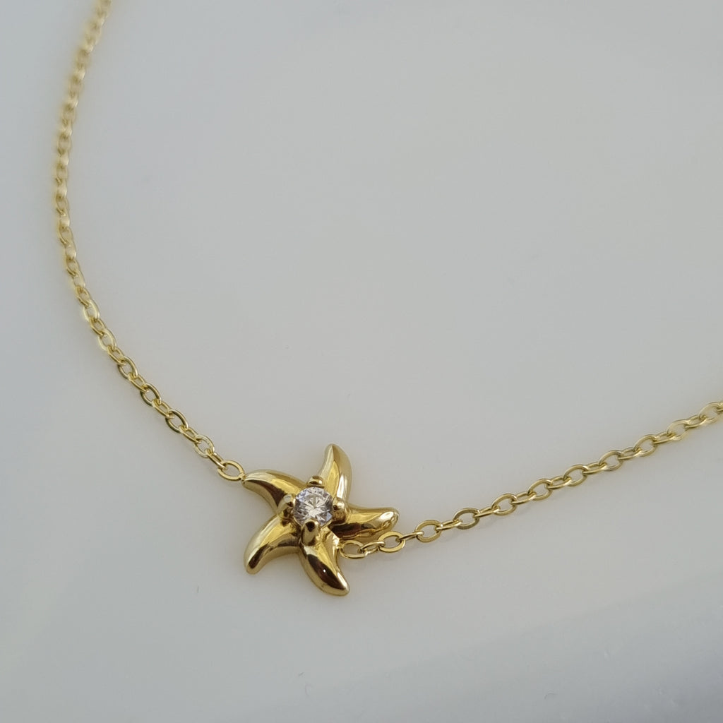 Treshire 18K gold plated Coastal Starfish bracelet with a center crystal on a fine gold chain, displayed on a white marble surface.
