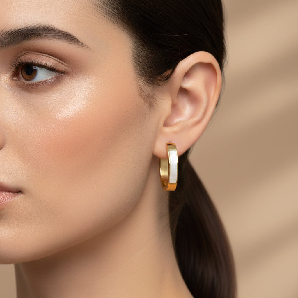 A woman with a sleek ponytail wearing 18K gold-plated rectangular huggie earrings featuring a luminous white iridescent inlay and a high-polish finish.