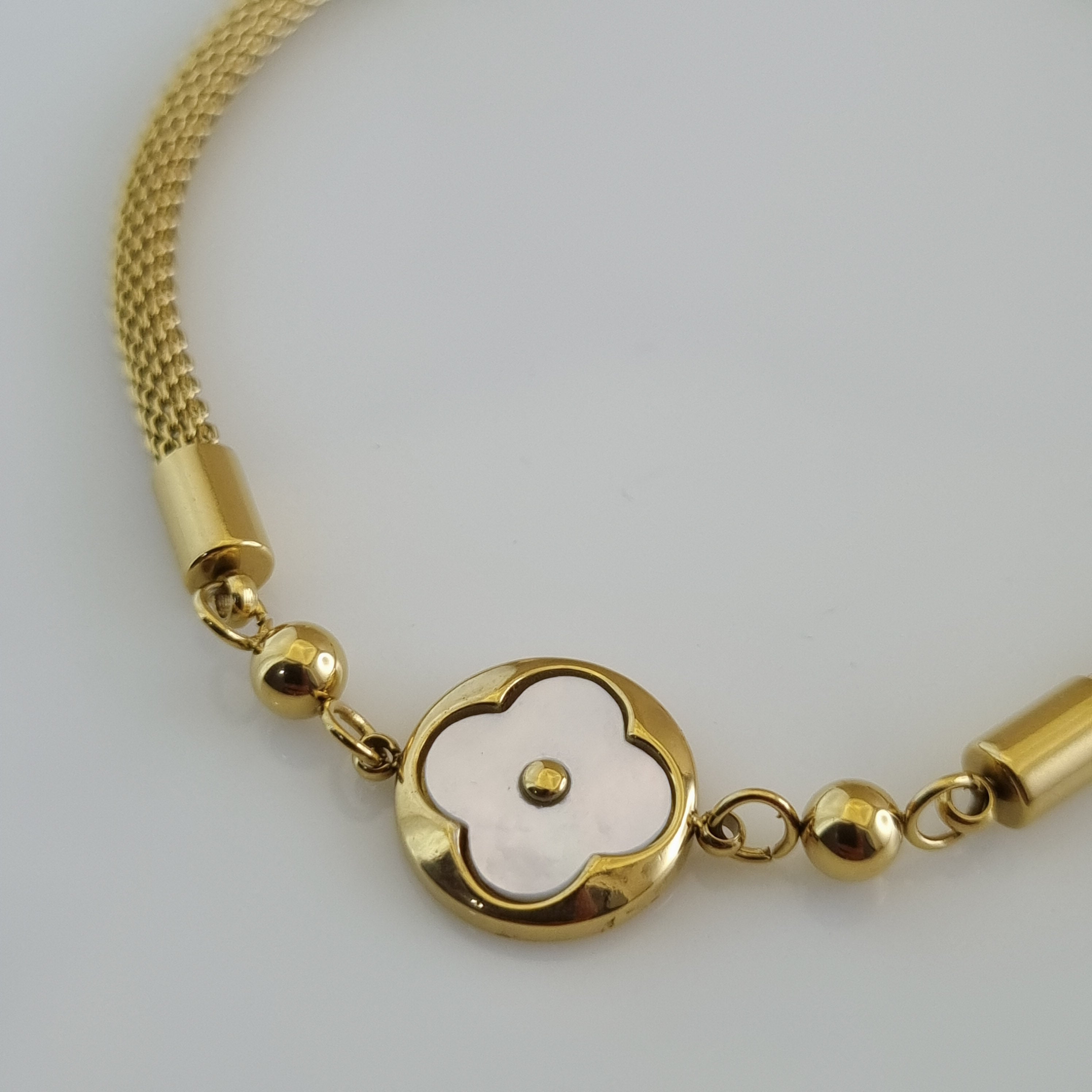 Treshire 18K gold plated mesh bracelet with a central Mother of Pearl clover charm and gold bead accents on a white display.