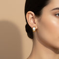 A woman with a sleek hairstyle wearing small, 18K gold-plated rectangular huggie earrings with a white iridescent inlay.