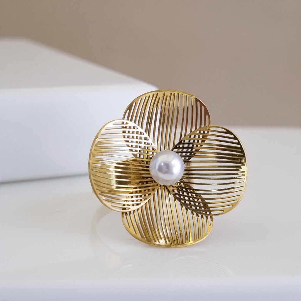 Gold flower-shaped brooch ring with a pearl center on a beige background