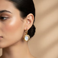 A woman with a sleek hairstyle wearing 18K gold-plated hoop earrings with a large, bezel-set iridescent moonstone drop and a high-polish finish.