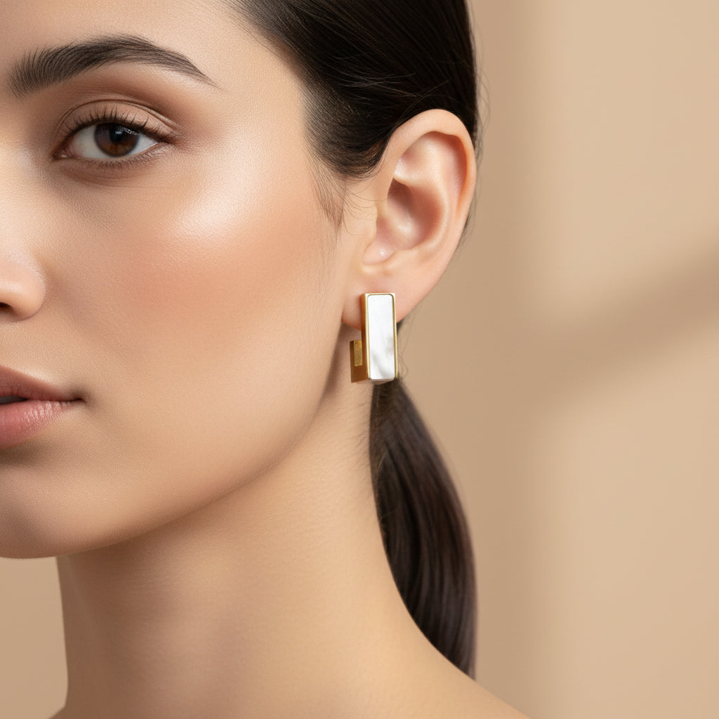 A woman with a sleek ponytail wearing 18K gold-plated vertical bar stud earrings featuring a white iridescent inlay and a high-polish finish.