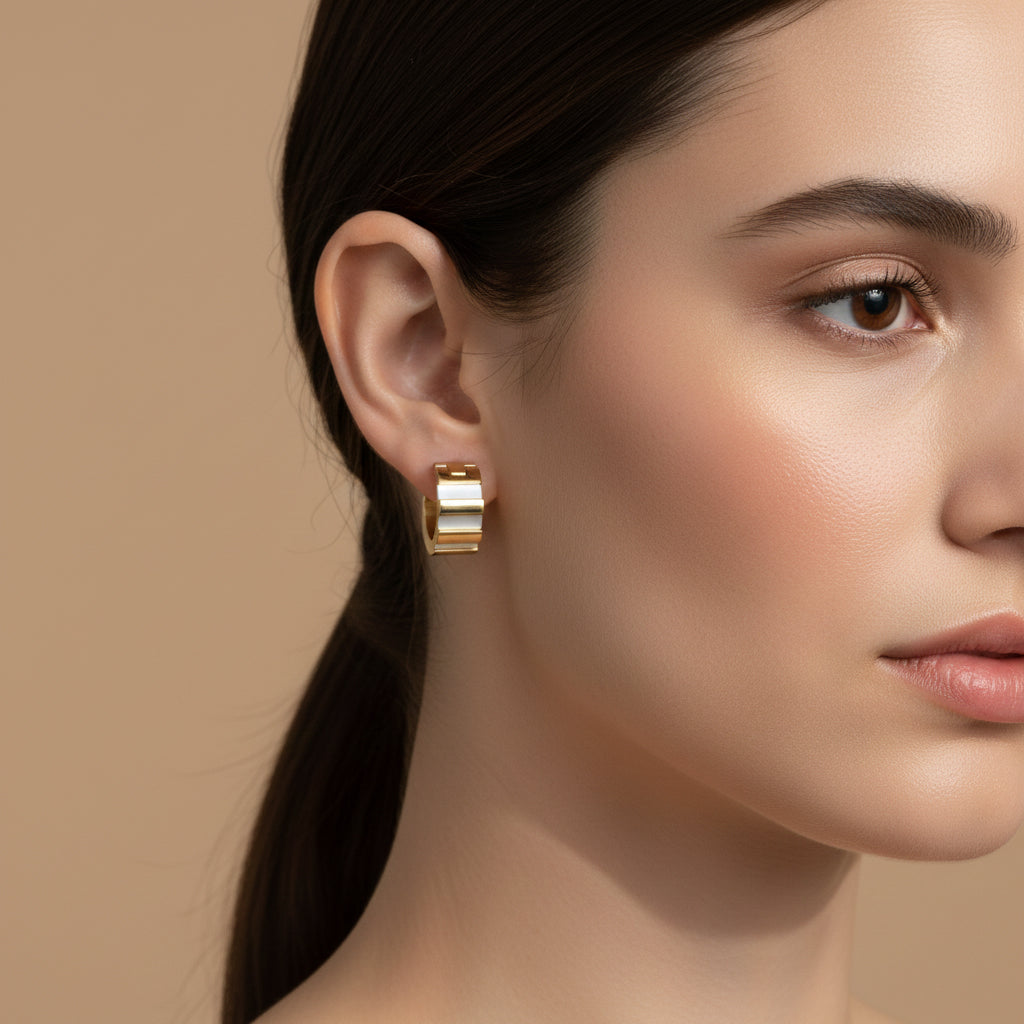 A woman with a sleek ponytail wearing 18K gold-plated rectangular huggie earrings featuring a recessed center with white iridescent inlays and a high-polish finish.