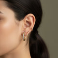 A woman with a sleek hairstyle wearing 18K gold-plated huggie hoop earrings featuring a continuous row of shimmering pavé crystals and a high-polish finish.
