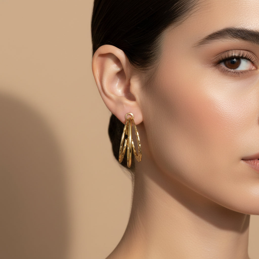 A woman with a sleek hairstyle wearing large 18K gold-plated triple-band hoop earrings featuring a mix of high-polish and hammered textures.