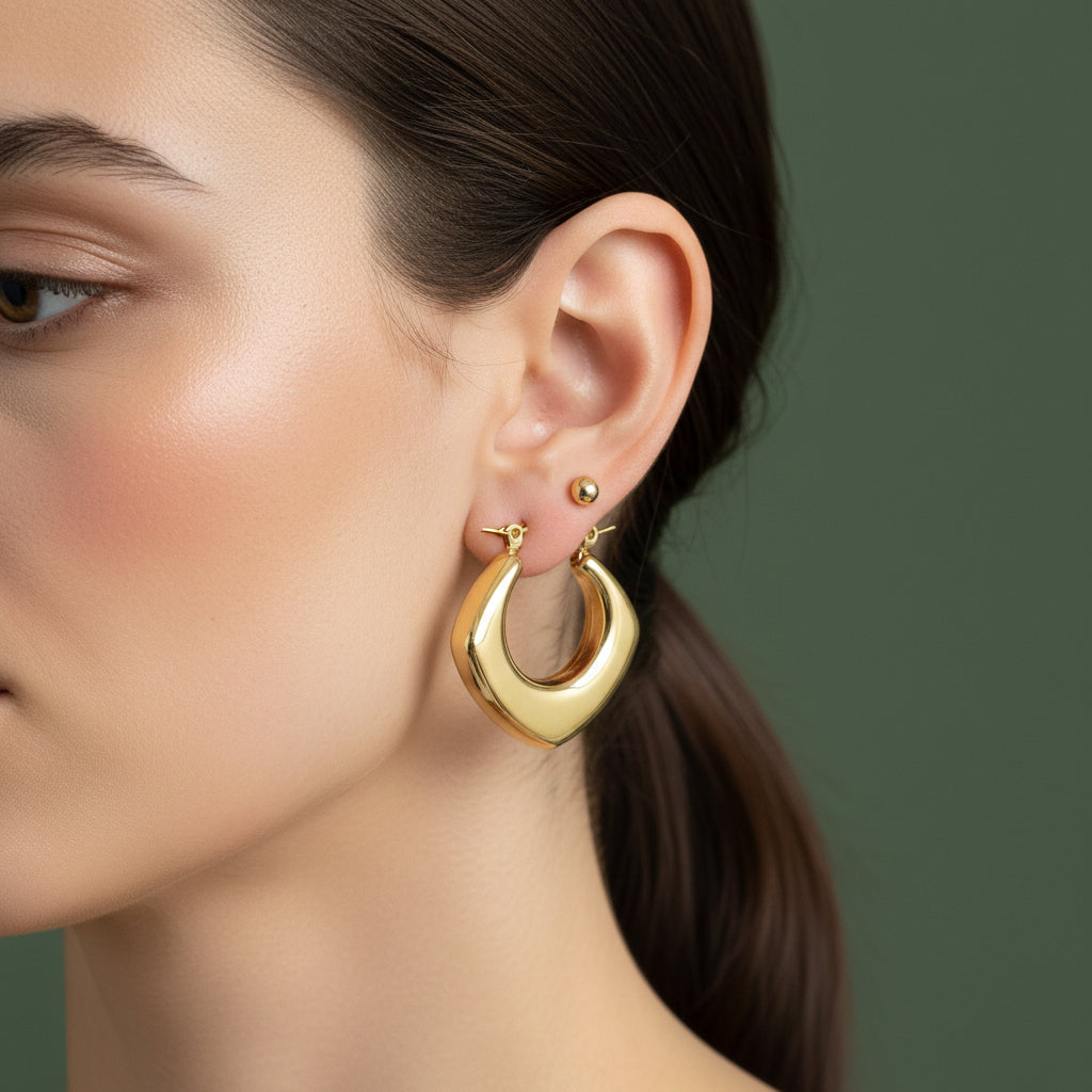 A woman with a sleek hairstyle wearing large, 18K gold-plated tapered crescent hoop earrings with a high-polish weighted design.
