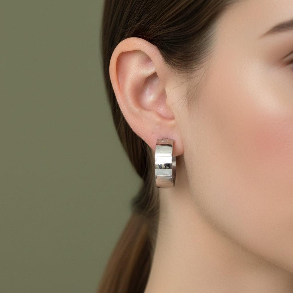 A woman with a sleek ponytail wearing large, 18K white gold-plated wide beam hoop earrings with a high-polish segmented design.