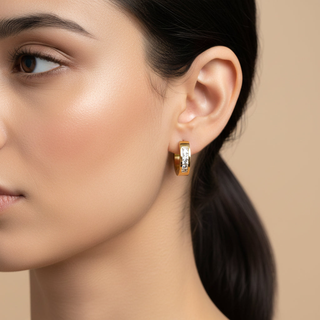 A woman with a sleek ponytail wearing 18K gold-plated rectangular huggie earrings featuring a vertical channel of clear crystals and a high-polish finish.