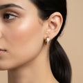 A woman with a sleek ponytail wearing 18K gold-plated rectangular huggie earrings featuring a vertical channel of clear crystals and a high-polish finish.