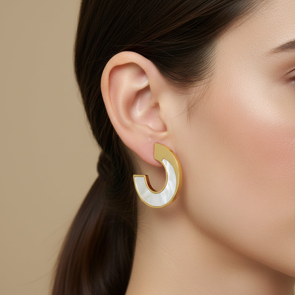 A woman with a sleek ponytail wearing 18K gold-plated wide open-arc hoop earrings featuring a white iridescent inlay and a high-polish finish.