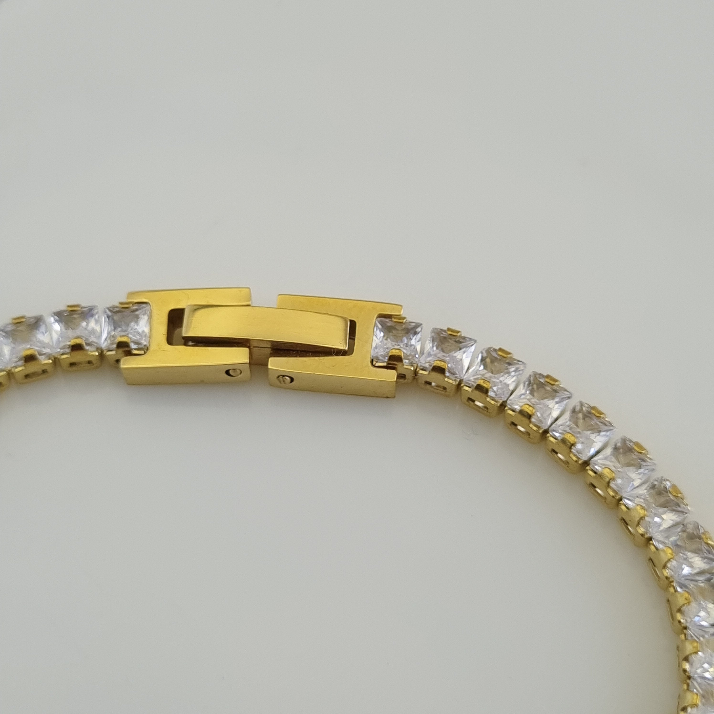 Gold bracelet with clear gemstones on a light gray background