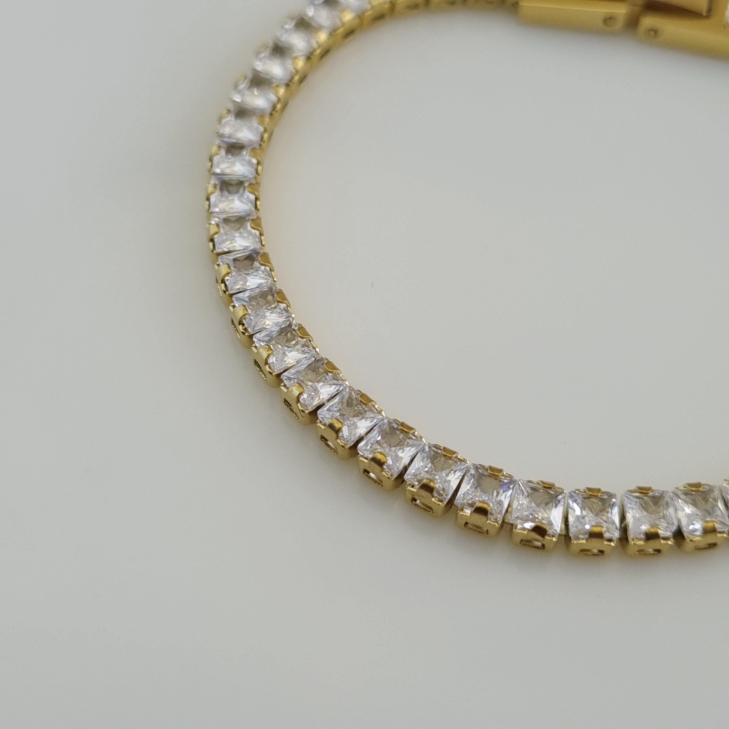 18K gold plated tennis bracelet featuring a continuous row of baguette-cut zirconia crystals and a secure hidden clasp.