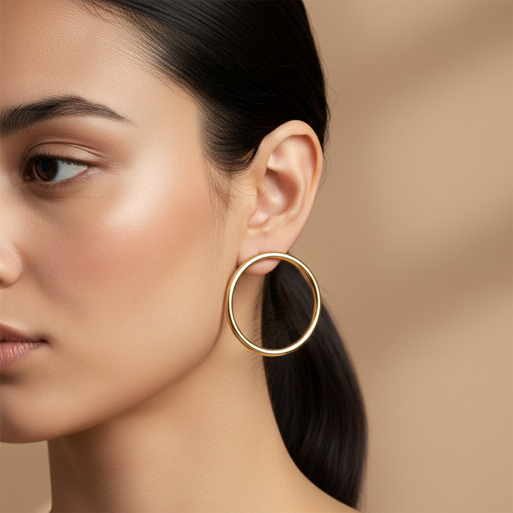 A woman with a sleek low ponytail wearing medium-sized, high-polish 18K gold-plated tubular hoop earrings.