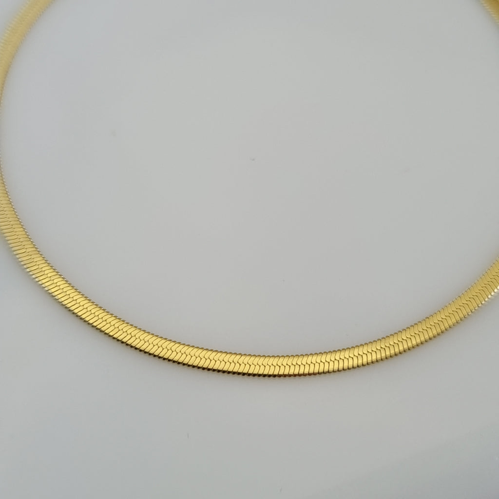 Treshire 18K gold plated Siena slim snake chain bracelet with a flat herringbone weave and heart tag on a white surface.