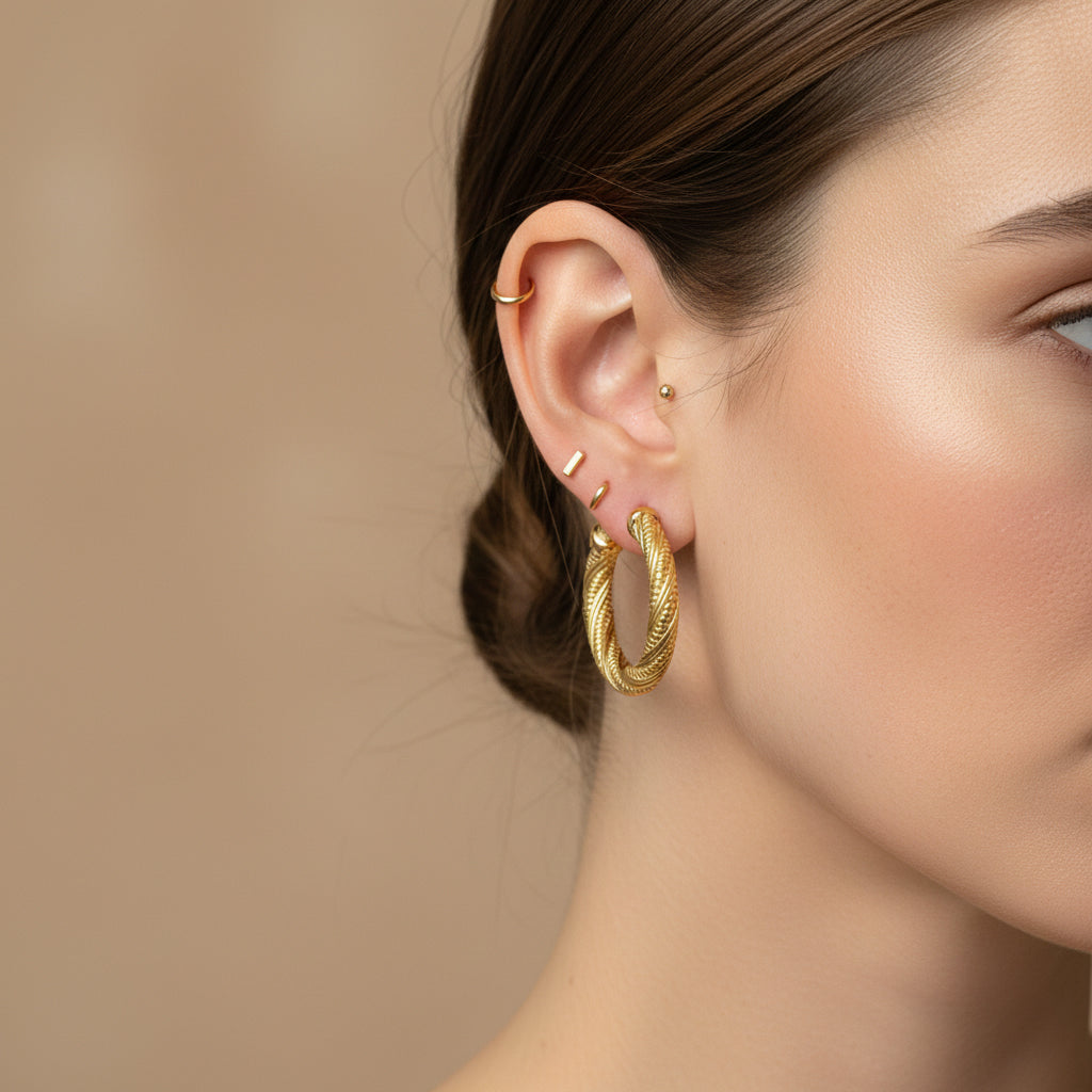 A woman with a sleek low bun wearing large, 18K gold-plated hoop earrings featuring an intricate braided rope texture and high-polish finish.