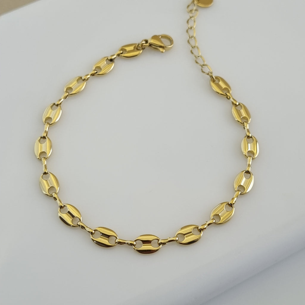 Treshire 18K gold plated Marina link bracelet with high-polish coffee bean style anchor links displayed on a white marble surface.