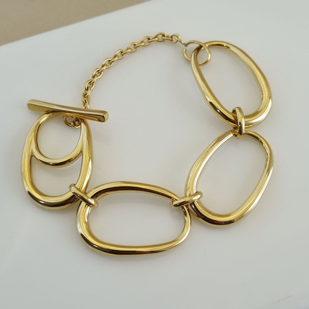 Treshire 18K gold plated bold bracelet featuring oversized sculptural ovoid links and a T-bar toggle clasp on a white surface.